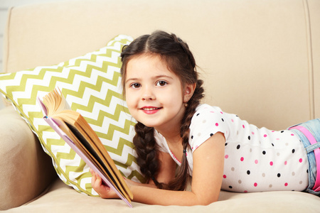漂亮的小女孩坐在沙发上用的书，关于家庭室内背景