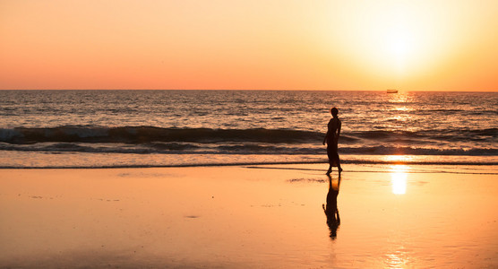 一个年轻的女孩，令人惊叹的日落期间的大海在海滩漫步的剪影
