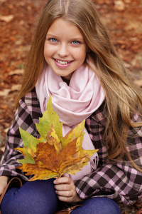 可爱的小女孩微笑着与枫树叶在手中