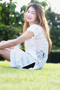 亚洲年轻漂亮的女人放松和坐在绿色的草地上