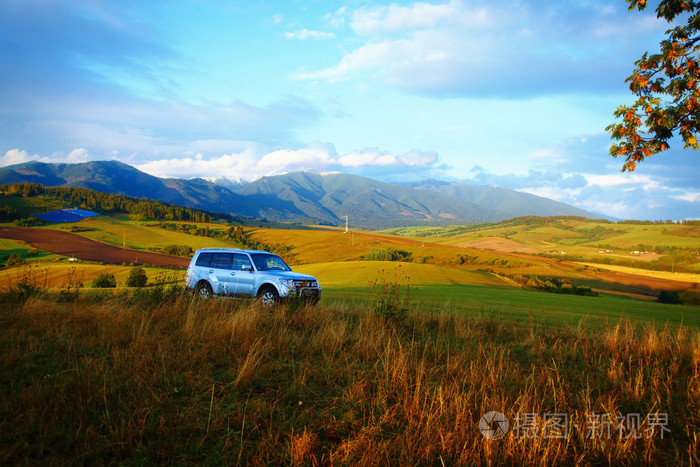 汽车在与雪山, 黄的, 绿的草甸景观.与背景上的太阳能发电设备.