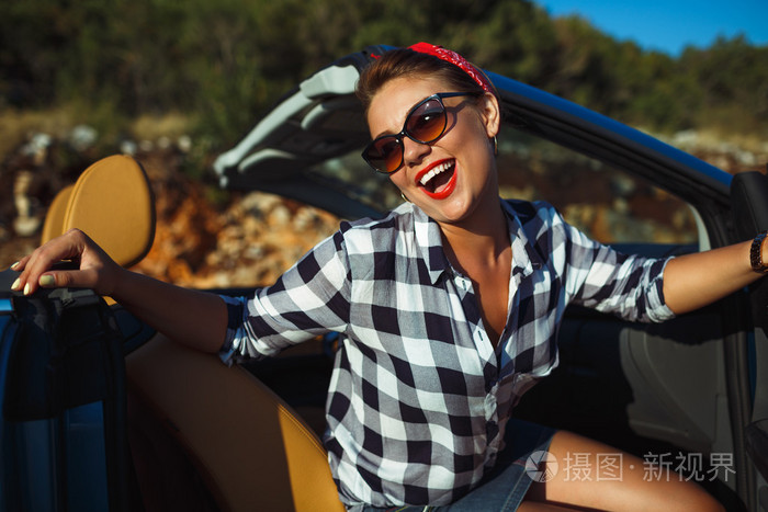 女人坐在敞篷跑车,享受旅行的路美丽针