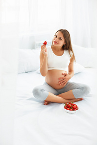 孕妇在家吃草莓。 健康的食物概念。