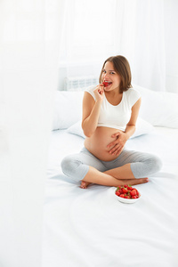 孕妇在家吃草莓。 健康的食物概念。