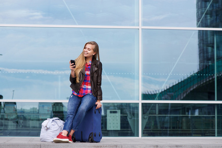 年轻的旅行坐在行李箱看手机上的女人