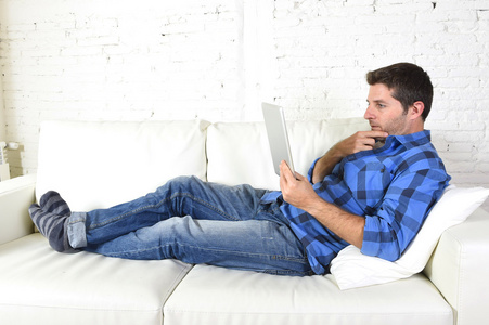 年轻漂亮的30多岁男人用数码平板电脑躺在沙发上