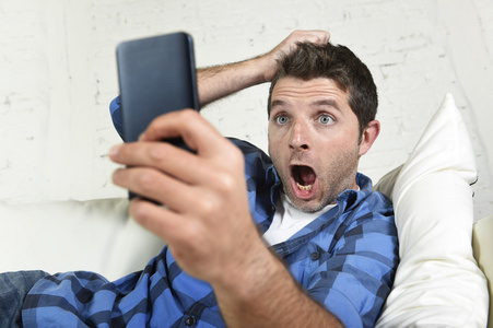年轻有魅力的男人躺在家里的沙发上，用手机上网