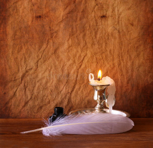 低调形象的白色羽毛，墨水池和燃烧的蜡烛在一个木桌上。