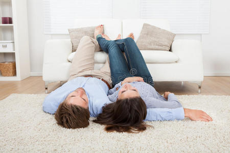 一对夫妇躺在地板上,双脚放在沙发上亚洲女人坐在地板上双脚靠拢