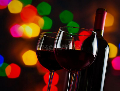 两个红葡萄酒玻璃杯在五颜六色的波基灯光背景下靠近酒瓶
