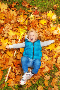 男孩笑着用耙子躺在秋叶上