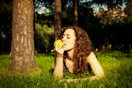 年轻漂亮的女人吃苹果在户外