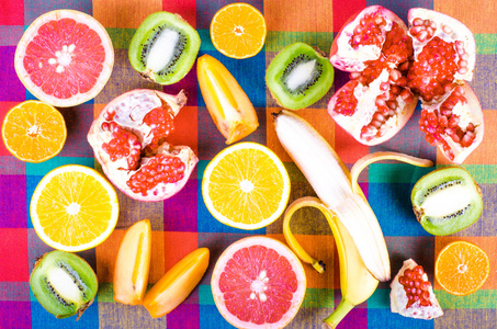 在五颜六色的格子厨房毛巾上享用新鲜水果。生食和素食饮食背景。橘子片, 子, 猕猴桃, 橘子, 香蕉, 柠檬, 苹果, 柚子, 石