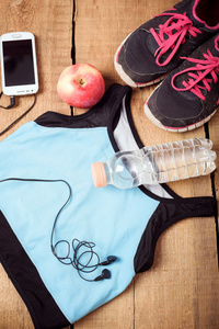 运动器材。运动鞋 水 苹果 蓝色上衣 智能手机和耳机上木制的背景。适合跑步的衣服