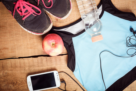 运动器材。运动鞋 水 苹果 蓝色上衣 智能手机和耳机上木制的背景。适合跑步的衣服