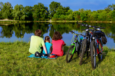 家庭自行车骑在户外，活动的父母和孩子骑自行车和放松附近美丽的河