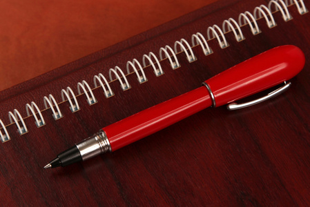 笔记本和一支红笔，躺在木桌上