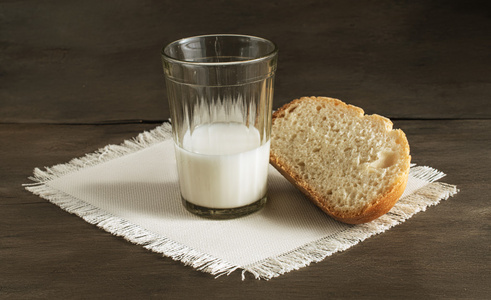 一杯牛奶和一条新鲜面包上亚麻餐巾放在木制的背景