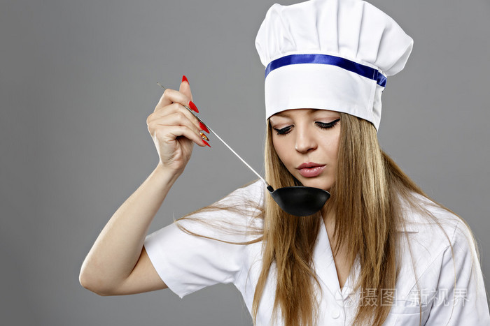女厨师拿着勺子从勺子吃在灰色的背景和目标