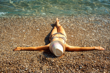 年轻女子在一顶帽子和比基尼躺在海滩上，在炎热的夏天