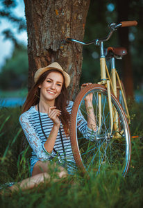 可爱的年轻女子在一顶帽子用一辆自行车在公园里