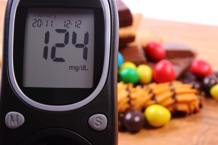 血糖仪与堆的甜食对木质的表面 糖尿病和不健康的食物