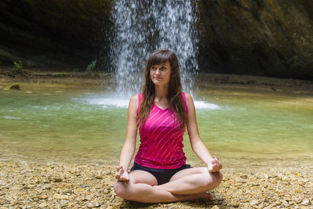 练瑜伽在瀑布附近的年轻白种的女性