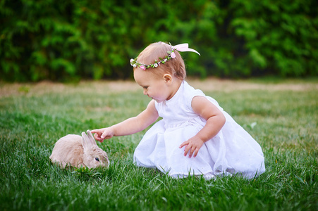 穿着白色连衣裙的小女孩和一只兔子在公园里玩