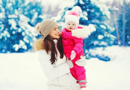 快乐微笑的母亲和孩子走在下雪的冬天森林