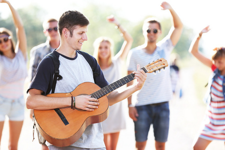 有魅力的年轻人在户外和跳舞的朋友玩吉他