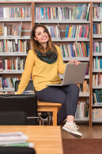 快乐的女学生工作与图书馆的笔记本电脑