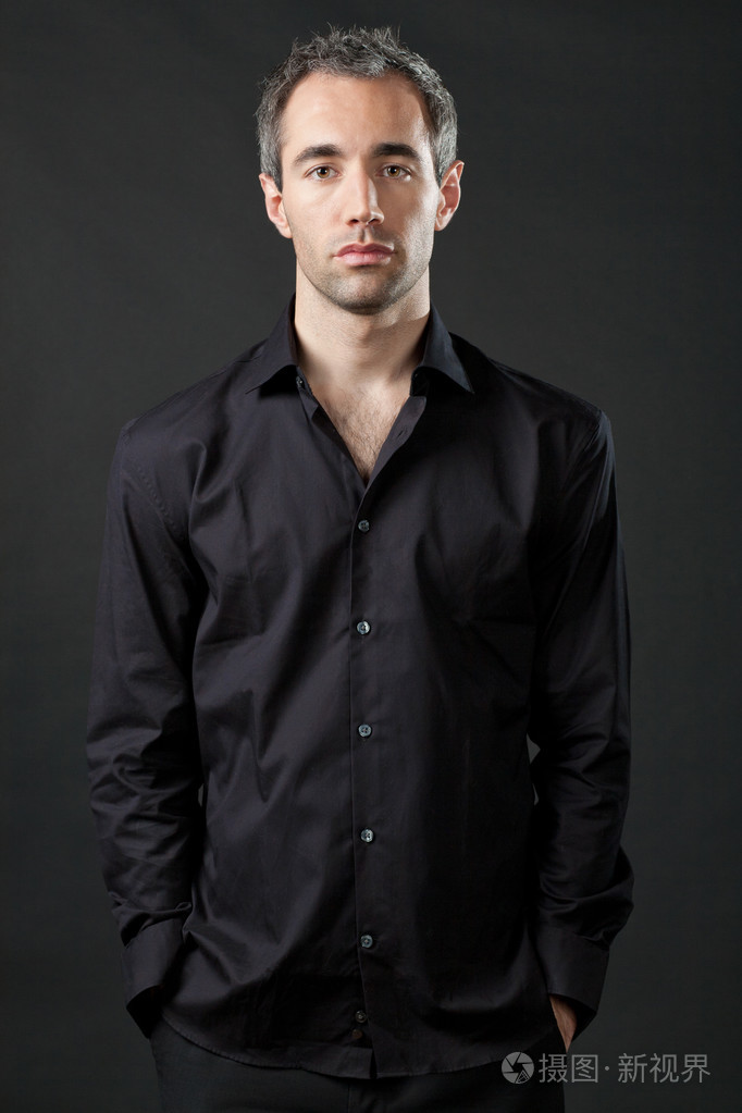 英俊的男人,在深色背景上的黑色衬衫摆姿势
