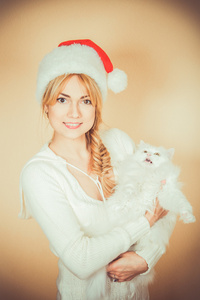 在圣诞老人的帽子的女孩拿着一只毛茸茸的白色猫
