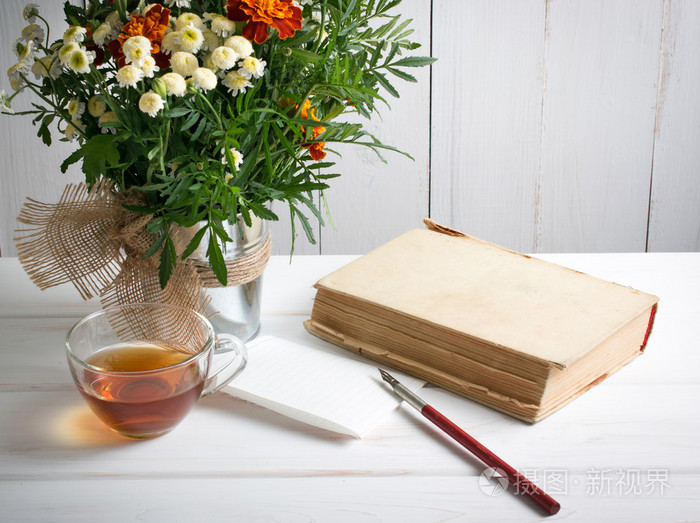 万寿菊鲜花花束用老书和杯茶和笔尖笔上