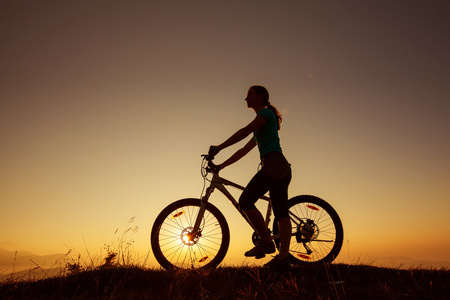 骑自行车的人女孩在日落时在山上