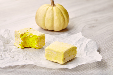 美味的两个方形的黄色糊状棉花糖在手工纸上咬