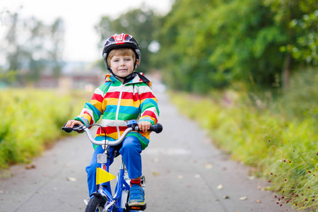孩子在红色安全帽驾驶在他的第一辆自行车上的男孩