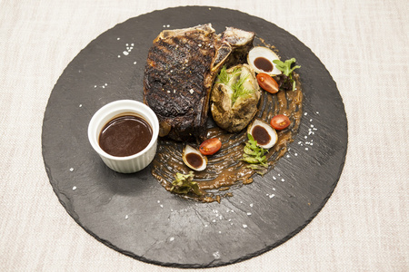 ribeye 牛排由大理石牛肉和蔬菜和烧烤酱制成。在一块黑色的石头上服务