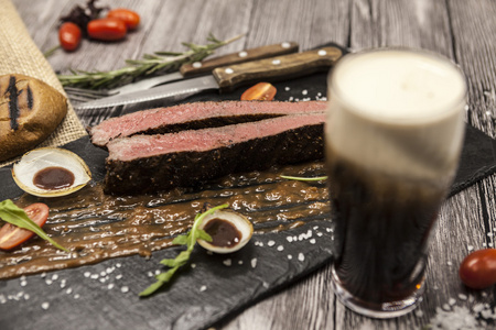 ribeye 牛排由大理石牛肉和蔬菜和烧烤酱制成。用叉子刀和啤酒在一块黑色的石头上食用