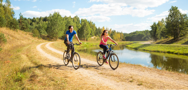 年轻幸福的夫妇在河边骑自行车