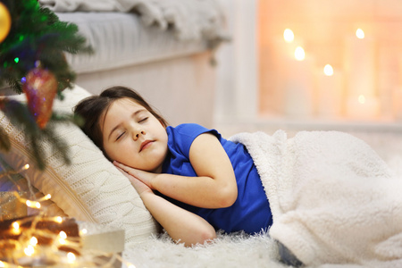 漂亮的小女孩睡在舒适的沙发上，在圣诞节装饰的房间