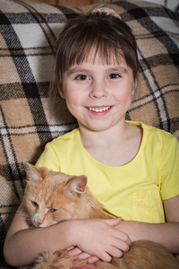 可爱的小女孩坐在一把椅子和拥抱红猫