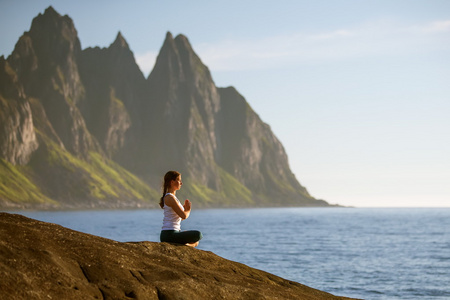 年轻女子正在练习瑜伽在挪威山之间