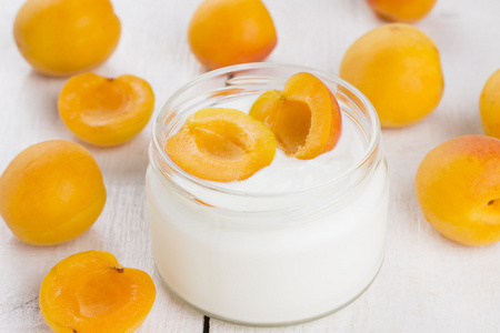 在玻璃罐子里用白色木制背景上杏子酸奶