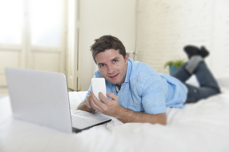 年轻有魅力的男人躺在床上用手机计算