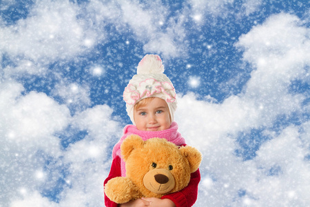在温暖的帽子和一件红色的毛衣与泰迪熊的小女孩