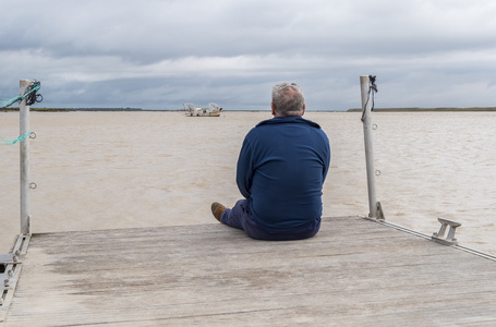 男子坐在面对河流的木码头上思考
