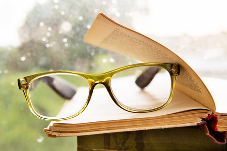老花眼镜和多雨的窗口上的书照片