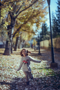 在秋天在城市公园里玩耍的小女孩