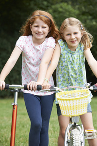 两个女孩在一起骑自行车和滑板车